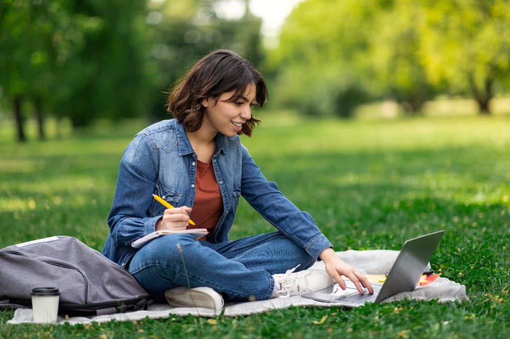 Student studying outdoors with a laptop and notebook